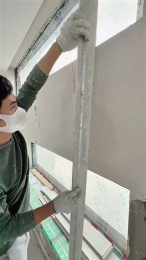 applying white plaster on the wall using a metal trowel to smooth the surface between two windows