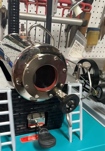 Wilesco D 18 steam engine with a blueish base plate that has been combined with a black boiler housing and silver-colored engine plate. Wilesco types D 20 and D 16, enhanced by a number of technical refinements. The engine plate has now been additionally fitted with a dynamo to supply the streetlight at the rear, between the boiler and engine, with current. The streetlight is modeled on an industrial streetlight from the turn of the century and shines on the flywheel during operation. Find this 