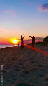 Two women dancing on the beach in front of the sunset. Vertical video