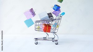 Multi-colored gift boxes fall into a shopping cart on a white background. 4k raw slow motion video. Filmed on high speed cinema camera, 1000fps.