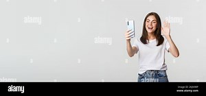 Friendly attractive girl saying hi, waving hand at smartphone during video call, having conversation Stock Photo - Alamy