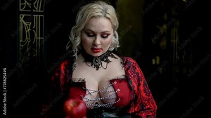 Close-up portrait of beautiful plus size blond woman wearing red dress with cleavage and holding red apple fruit. Soft focus. Real time handheld video. Beautiful people theme.
