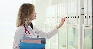 Focused female doctor looks at ring binders for necessary document case with data about patient. Organized folder structure and archive on light rack slow motion