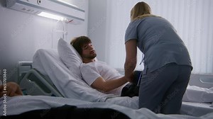 Female nurse comes to resting in bed patient, measures blood pressure and asks health care questions. Man fully recovering after successful operation. Medical personnel does checkup in hospital room.