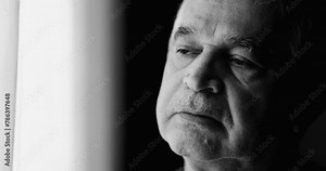 Introspective contemplative elderly man with unshaven wrinkled close-up face struggling with mental illness in solitary expression in black and white. Melancholic emotion in old age