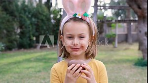 Easter egg hunt. Excited emotion surprise adorable child girl with dirty mustache mouth in bunny ears rabbit costume hold and eat Easter chocolate egg. Children positive emotions. Kid happy Easter