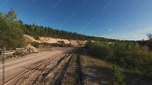 Aerial drone footage of a logging site or construction area near a forest. The scene shows piles of logs and machinery tracks, with a sandy terrain surrounded by trees under a clear sky. 4k footage Stock Video