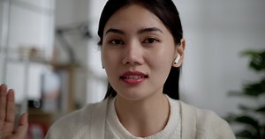 Locked close up shot, Face of Young vlogger female use earphones looking at camera and talking on live streaming at home