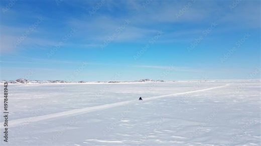 Lateral drone tracking shot following a snowmobile along a winter trail on the frozen sea ice of Frobisher Bay.