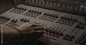 Lighting technician's hand comes into shot and adjusts multiple sliders on professional lighting control desk