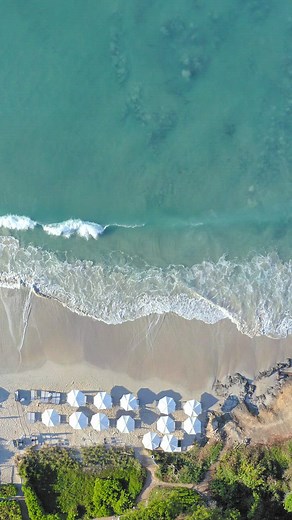 Aerial view of the beautiful turquoise waves crashing on the sand beach with white umbrellas - Free Stock Video