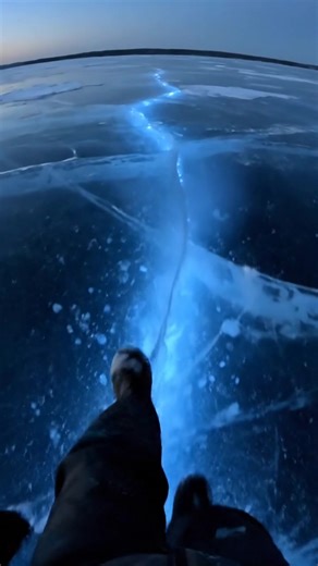 Blue cracks in the ice flicker with a faint internal light, running like glowing veins beneath the frozen surface of the lake. The light shifts and pulses slowly, tracing patterns that seem alive under the translucent blue. Each movement sends a soft shimmer across the ice, cold, silent, and impossibly beautiful. #earthimpacts #fblifestyle #glacialwonder #frozenlight #earthmagic This content isn’t real — it’s a simulated ‘what if’ scenario created by AI for visual exploration. | Earth Impacts