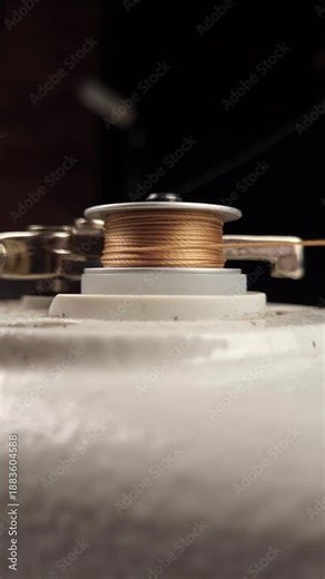 Sewing machine bobbin winder, golden thread winding onto bobbin on black background.