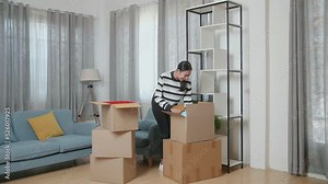 Young Asian Woman Moving Into A New House Taking Stuff Out Of The Cardboard Box And Decorating The Habitat Bookcase