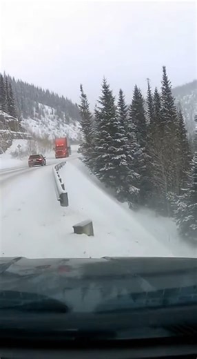 Semi Loses Control on Icy Mountain Curve, Trailer Slides Off Roadway Colorado Rockies — A winter drive through a mountain pass turned dangerous when a semi truck lost traction on an ice-covered curve, sending its trailer sliding off the roadway and into the trees as nearby drivers struggled to stop. Dashcam footage shows cars creeping along the snow-packed road when the tractor-trailer ahead begins to drift. The trailer swings wide, scraping past the guardrail before dropping off the edge and co
