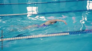Sportswoman swimmer swims along the swimming lane in the pool in freestyle. A slender beautiful woman performs training exercises before a competition. Fitness training in a pool.