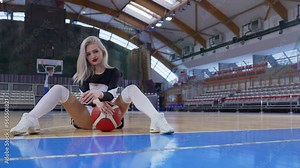 Cheerleader sitting on the floor with legs spread and a basketball between legs. High quality 4k footage