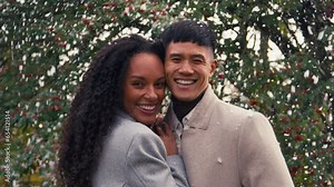 Loving young couple wearing coats standing outside and laughing as snow falls on winter countryside