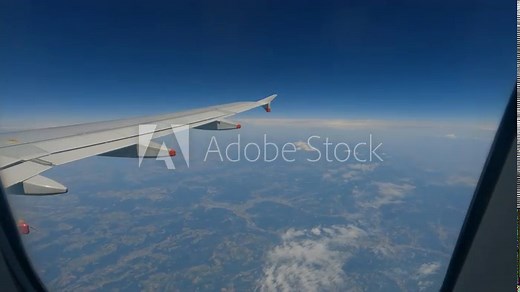 CLOSE UP: Male passenger looking out through the airplane window during flight. A young tourist traveller enjoys beautiful views of the clouds and landscape far below while flying high above Europe.
