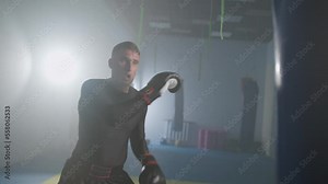 Aggressive fighter trains his kicks and punches in the boxing gym, a man boxer beats a punching bag, 4k slow motion.