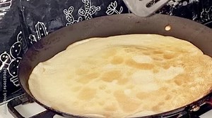 Large round pancake in a frying pan. Cooking smoke rises from the pancake. Pancakes with holes. Maslenitsa. Russian tradition. Cooking.