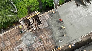 Group of construction workers in hardhats and reflective vests pouring wet screed using hose from concrete pump into reinforced beams at building site. Aerial view