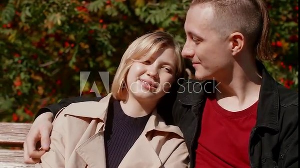 Young couple sharing intimate moments while sitting on park bench, experiencing deep connection amid autumn foliage and warm sunlight, radiating mutual affection and peaceful happiness