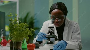 Portrait of pharmaceutical woman putting slide under microscope examining biological sample for medical experiment. Biologist analyzing organic agriculture plants in microbiology scientific laboratory