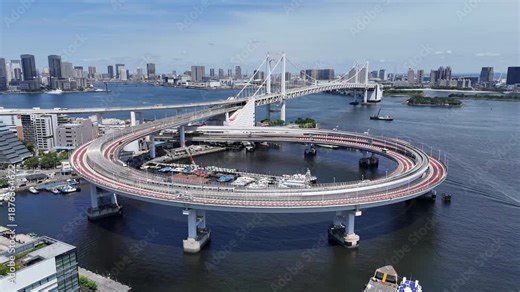 Flight over Rainbow Bridge loop interchange in Tokyo Bay with urban skyline and traffic