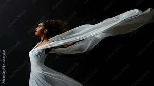 Woman in a flowing white dress poses elegantly with a billowing white fabric against a dark backdrop. The fabric swirls around her, enhancing the sense of grace and movement