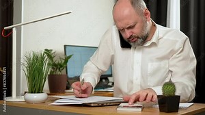 Overworked businessman, multitasking office worker, simultaneously talks on phone and checks financial data. Resilience in finance accounting. Mature age, middle age, mid adult man working at home