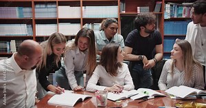 In a bustling university library, a group of diverse college students gathers around a table, engaged in earnest consultation with their professor. This scene embodies the essence of the university