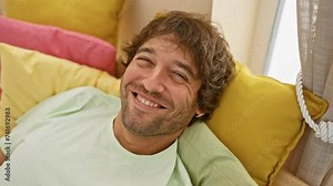 Hilarious young caucasian man puffing cheeks indoors, making funny face expressions at home, wearing pyjama in the bedroom room. crazy mouth air puff, amusing guy's gesture.