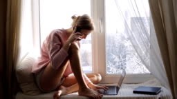 Woman working on her laptop and talking on her phone sitting on...