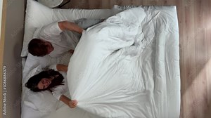 A happy young couple in their cozy bedroom, smiling and relaxing together in a warm ambiance before sleep. A peaceful and harmonious bedtime routine for two young adults. Happy couple in love to bed
