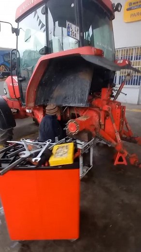 Mechanic Repairing a Red Tractor in Workshop