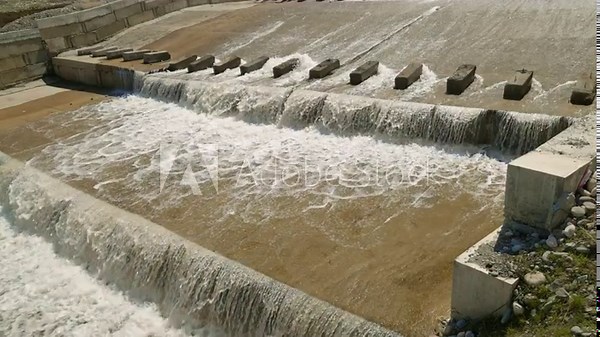 row of chute dentate blocks in concrete water spillway channel slope slowing down the flow of water running down.