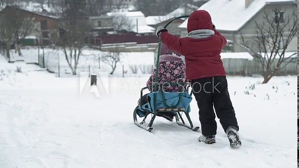vacation, game, family concept - slo-mo authentic Two happy preschool toddler kids siblings in hats and mittens sledding and rolling each other. snowfall in cold season weather in winter park outdoors