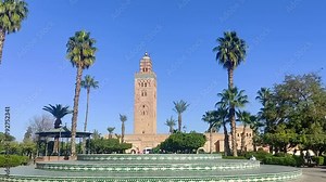 Historical sandstone tower in Morocco between palm trees in strong sun and balmy sky