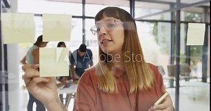 Designer, woman and writing sticky note by glass with thinking, vision or brainstorming in office. Graphic design, paper and pen by moodboard for planning, project management or creativity at startup