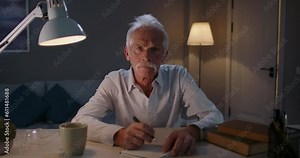 Old pensioner even in his old age aspiring to knowledge. Old student, 50-60 years old man studies from home. Online courses for all ages, advanced training online, male student writes down lecture.