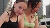 Middle aged mom and teen daughter sitting on sea beach and playing...