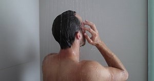 Man in shower washing hair showering in bathroom at home. Unrecognizable person from behind rinsing shampoo and conditioner from hair in warm bath with modern bathroom.