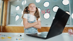 Cute girl using laptop programing software while looking and laughing at camera. Pretty child smiling while giving thump up with funny innocent mood in Stem class. Smart student portrait.Erudition.