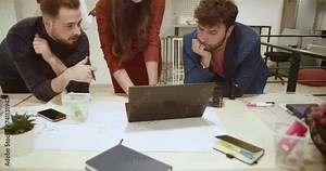 Three focused colleagues collaborate and discuss ideas around a laptop in a well-lit contemporary workspace, exemplifying teamwork and engagement in their collaborative efforts.