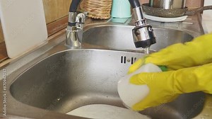close up young woman is washing dishes while doing cleaning at home. Housewife, daily house cleaning, routine. woman in protective gloves with sponge spray in kitchen. Puts dirty dishes in the sink