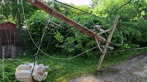 Power line completely destroyed by a fallen tree following severe storms and high winds. The wooden pole has been snapped in half created dangerous conditions and a power outage. Midwest, USA.