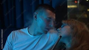 A young couple smokes a hookah in a night club, releasing a lot of smoke
