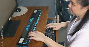 Asian woman with blindness disability using computer with refreshable braille display or braille terminal a technology assistive device for persons with visual impairment in workplace, handheld shot.