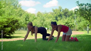 Push ups exercise. Young women doing push up exercise. Two woman doing pushups exercise in park. Woman pushing on green grass. GIrlfriends fitness training. Multi racial girls workout outdoor